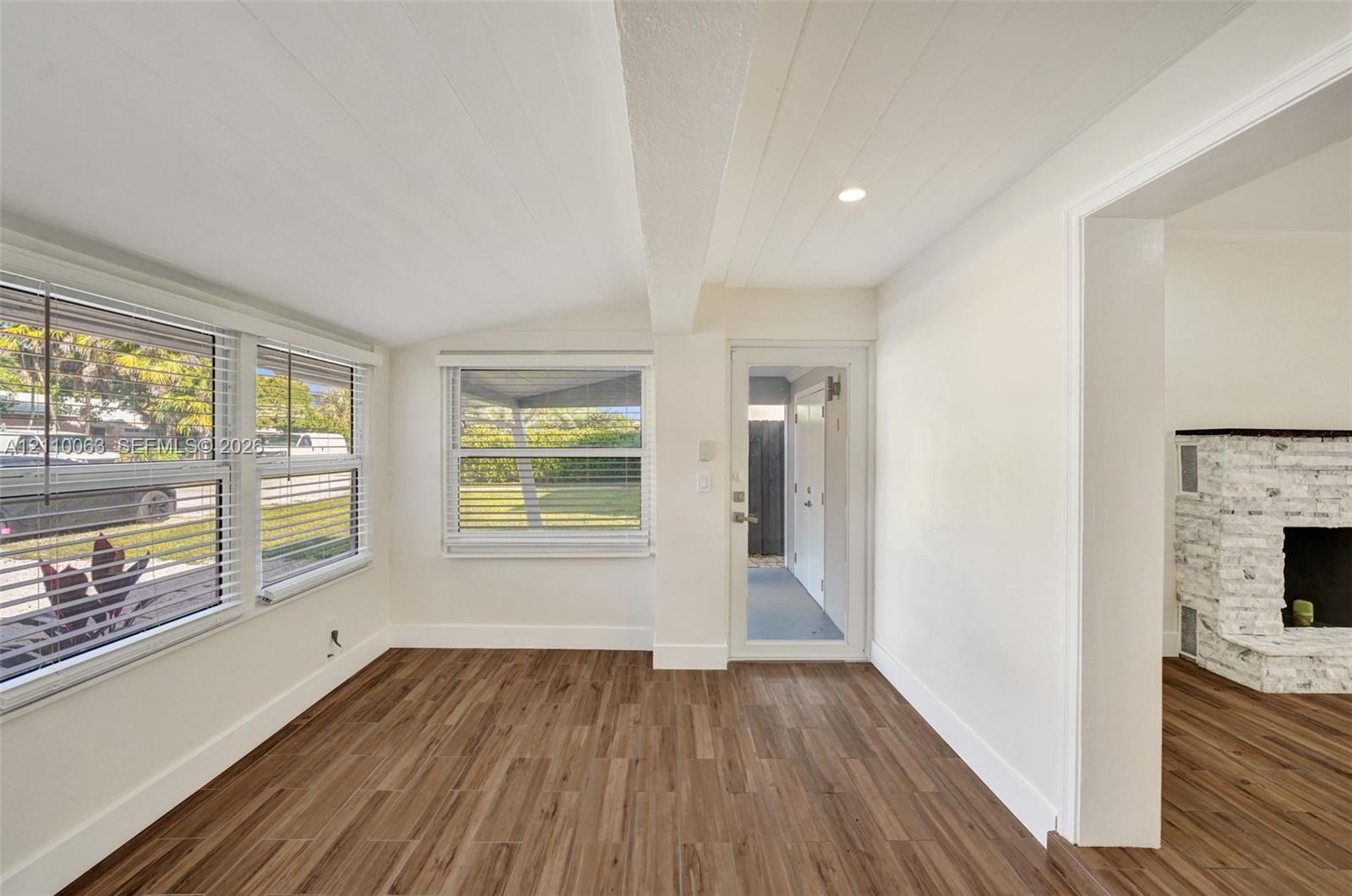 Wood-finish flooring, white plank-style ceiling, multi-pane windows, glass-panel exterior door, and a whitewashed brick fireplace Wood-finish flooring, white plank-style ceiling, multi-pane windows, glass-panel exterior door, and a whitewashed brick fireplace