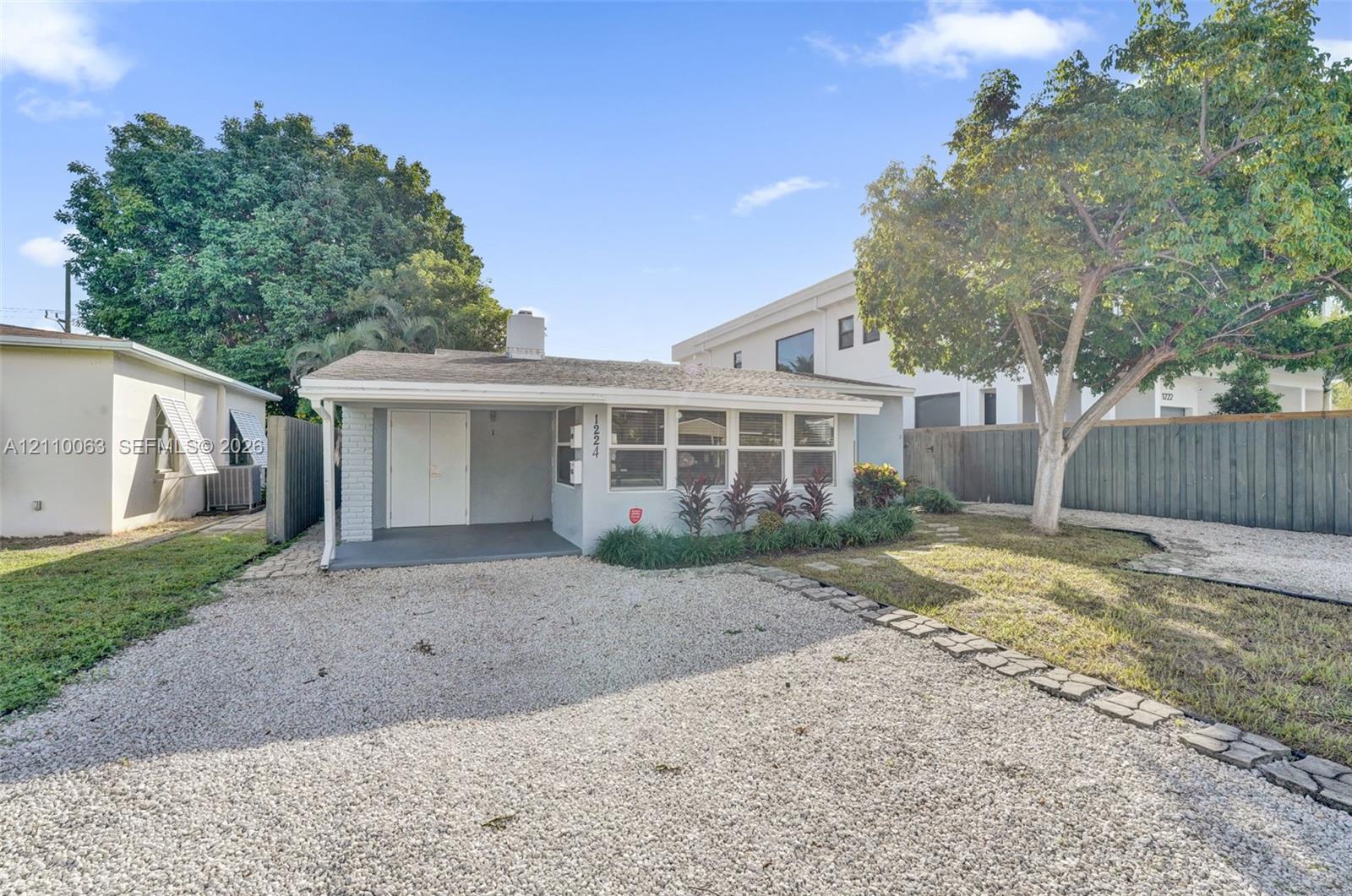 Single-story exterior featuring a covered entryway, light-toned painted brick, multi-pane windows, and a gravel driveway bordered by stone pavers Single-story exterior featuring a covered entryway, light-toned painted brick, multi-pane windows, and a gravel driveway bordered by stone pavers