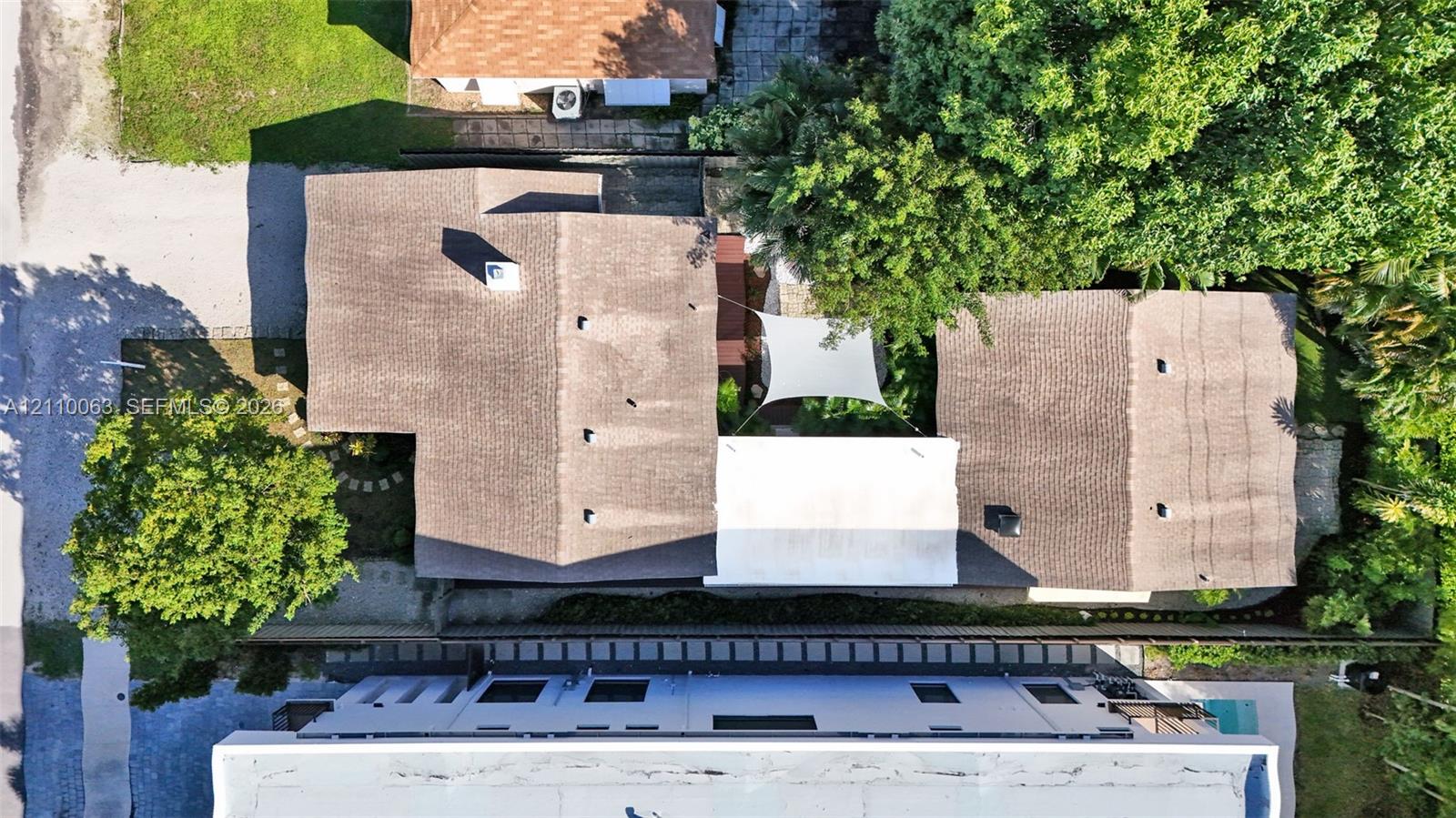 Aerial perspective of a multi-structure property featuring shingle roofing, mature trees, and a private courtyard area with a shade canopy Aerial perspective of a multi-structure property featuring shingle roofing, mature trees, and a private courtyard area with a shade canopy
