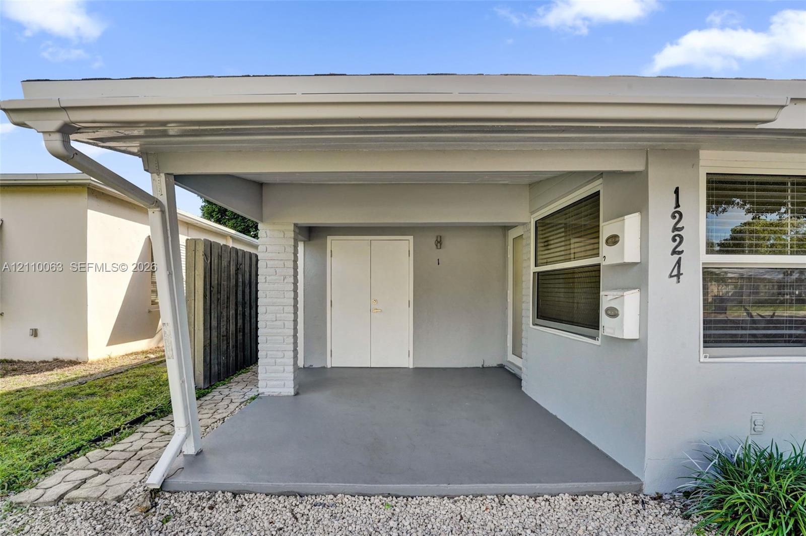 Covered entryway featuring a smooth concrete porch, white double-entry doors, painted brick accent column, and wall-mounted metal mailboxes Covered entryway featuring a smooth concrete porch, white double-entry doors, painted brick accent column, and wall-mounted metal mailboxes