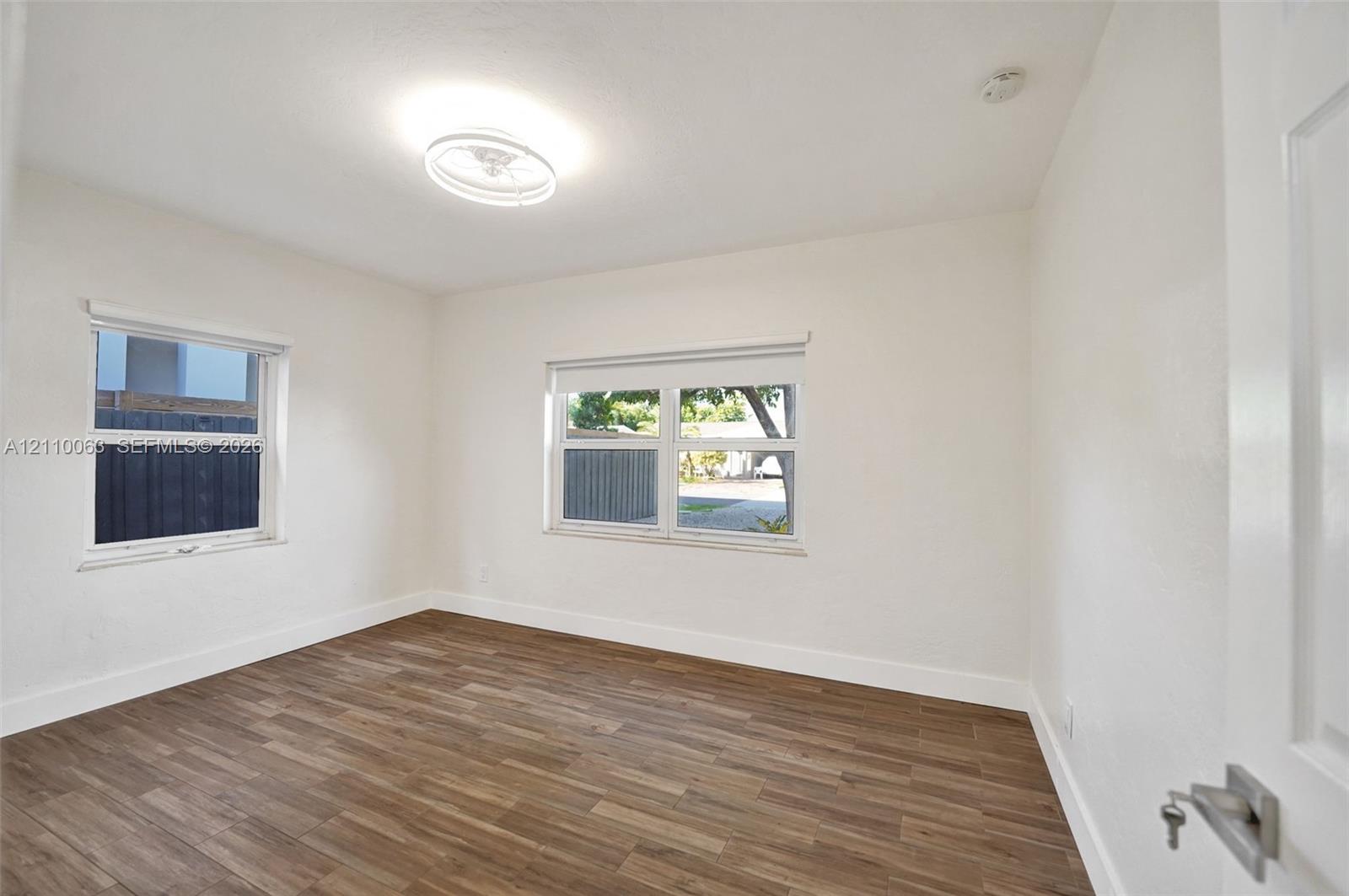 Room featuring wood-finish flooring, white walls, dual windows, and a flush-mount circular LED light fixture