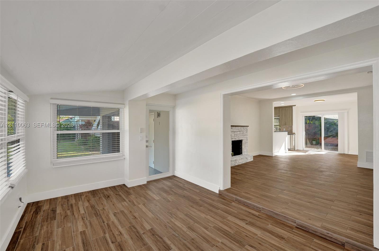 Interior space featuring wood-finish tile flooring, exposed structural beams, a brick fireplace, and sliding glass patio doors Interior space featuring wood-finish tile flooring, exposed structural beams, a brick fireplace, and sliding glass patio doors
