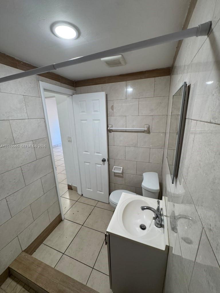 Bathroom featuring light-toned, large-format wall tile, floor tile, a white vanity with an integrated sink, and a wall-mounted mirror