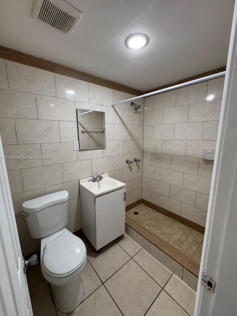 Full-height, large-format tile wall cladding, walk-in shower with integrated threshold, pedestal-style vanity with single-basin sink, and neutral ceramic tile flooring