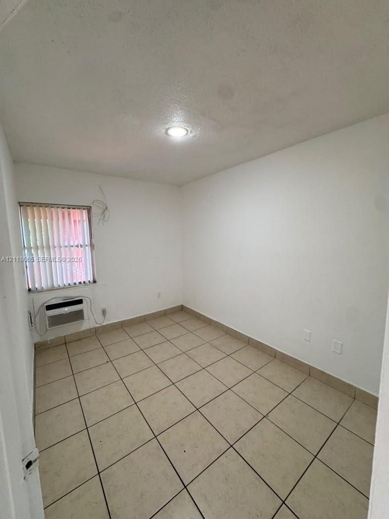 Room featuring neutral tile flooring, recessed ceiling lighting, and a wall-mounted climate control unit