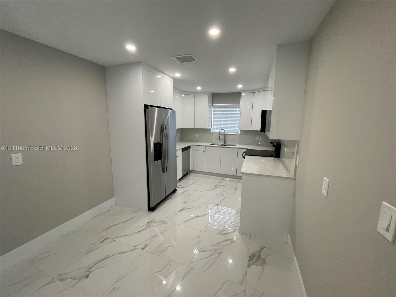 Large format, stone-finish tile flooring, recessed ceiling lighting, dual French doors providing exterior access, and a kitchen featuring built-in cabinetry