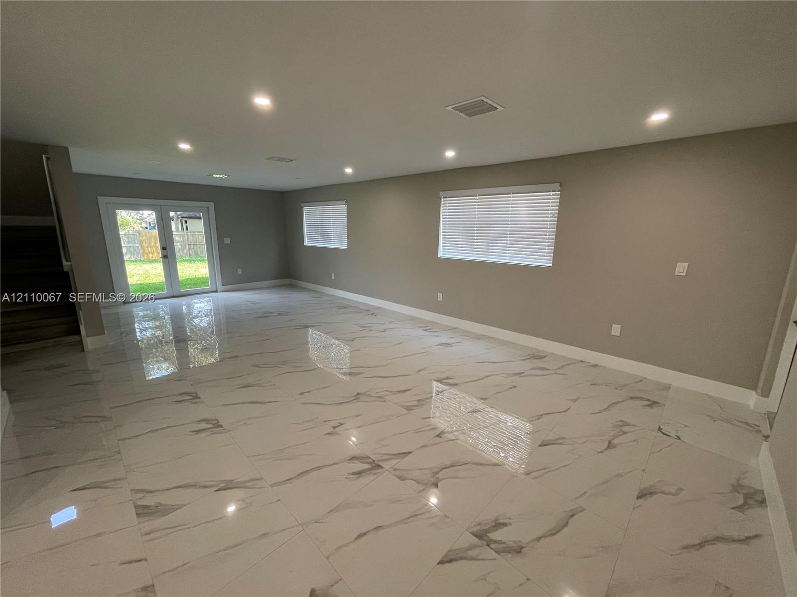Open interior space featuring polished stone-finish tile flooring, recessed ceiling lighting, and double glass-paned doors