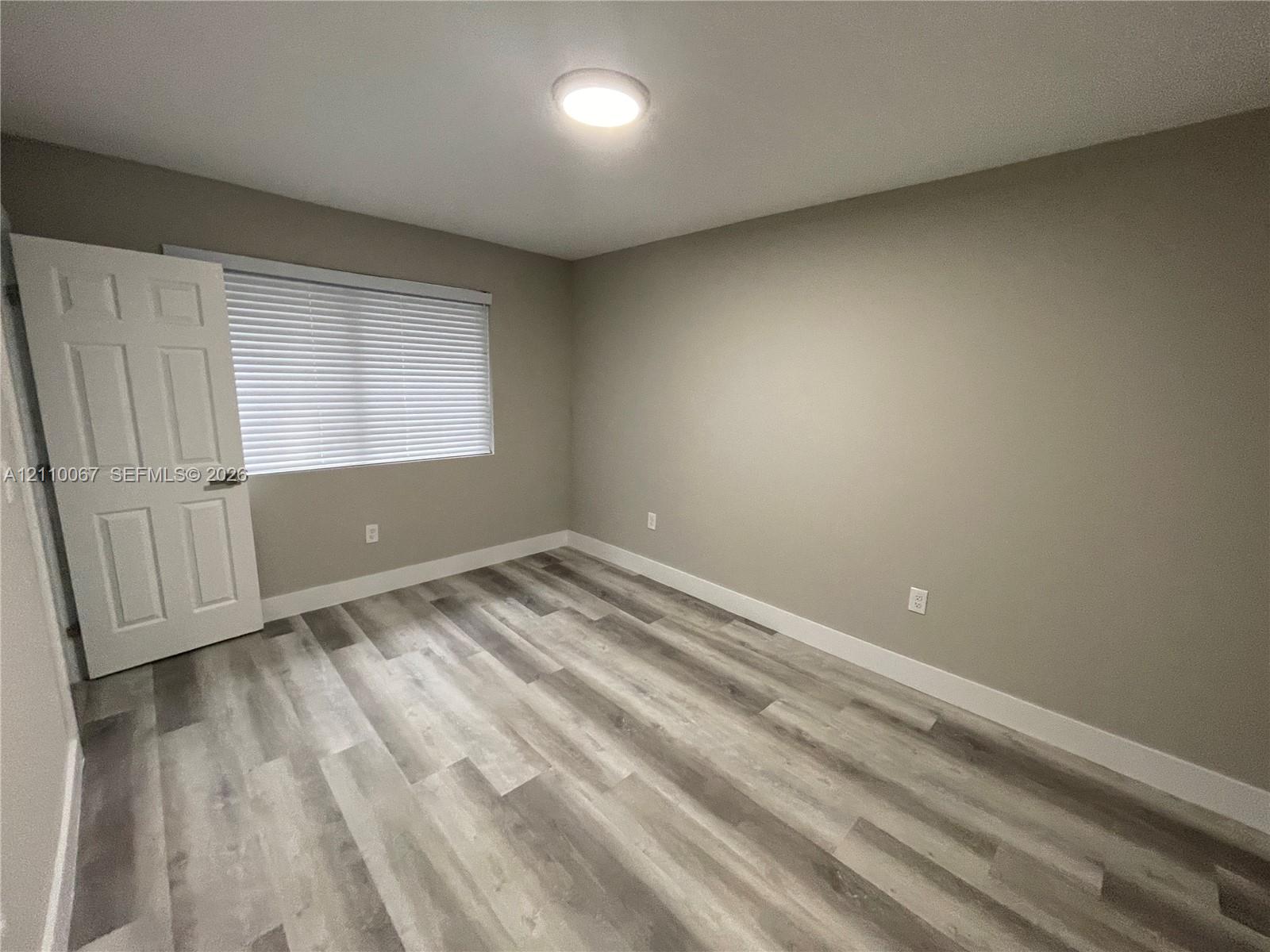 Bathroom featuring wood-finish flooring, a vanity with a solid surface countertop and undermount sink, a framed wall mirror, and a tub shower combination with large-format wall tile and a built-in recessed niche