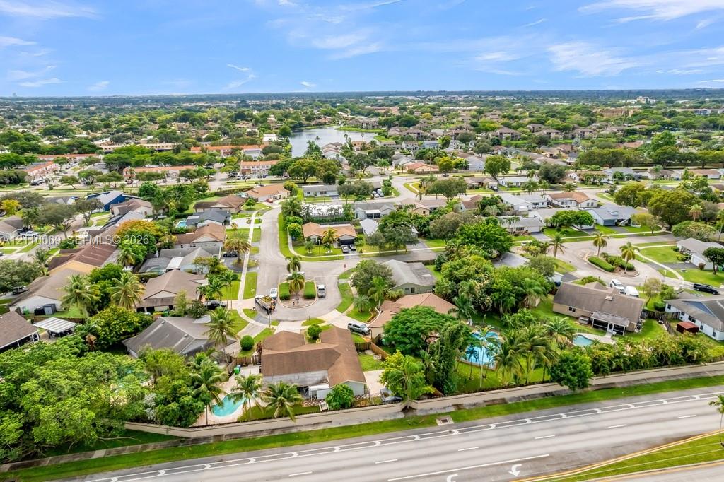 Aerial perspective of a residential neighborhood featuring mature landscaping, winding paved streets, multiple swimming pools, and residential structures with shingle roofing