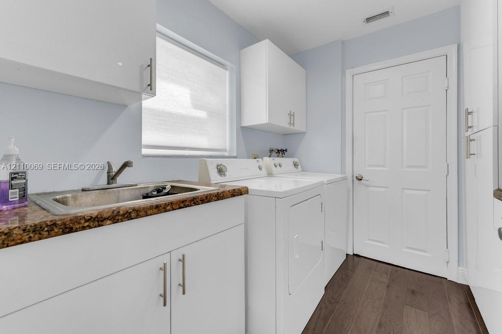 Laundry room featuring high-gloss white cabinetry, a stone-patterned countertop, an integrated stainless steel sink with a high-arch faucet, and wood-finish flooring