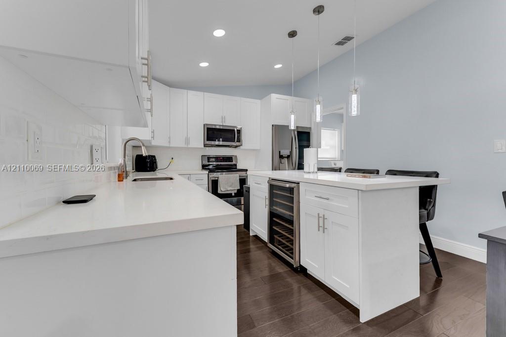 Kitchen featuring white cabinetry, quartz countertops, a central island with a built-in wine cooler, wood-finish flooring, and pendant lighting