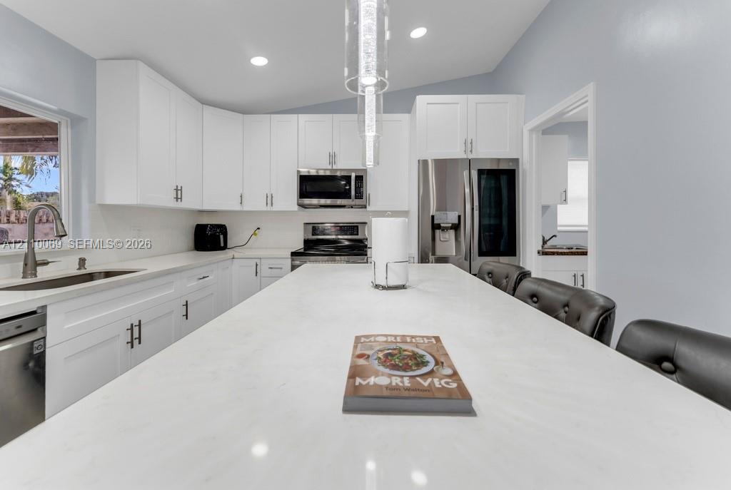 Kitchen featuring white shaker-style cabinetry, a quartz-surfaced center island, stainless steel appliances, recessed lighting, and a dual-basin undermount sink with a high-arch faucet