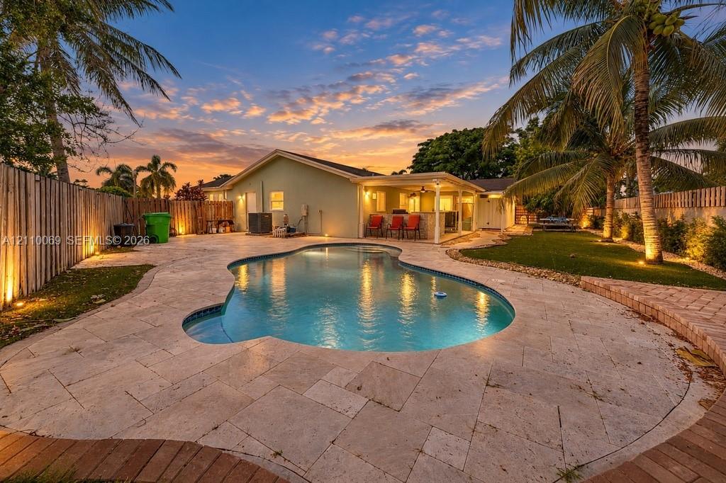 Outdoor living area featuring a freeform swimming pool, stone paver patio, covered lanai, and fenced perimeter