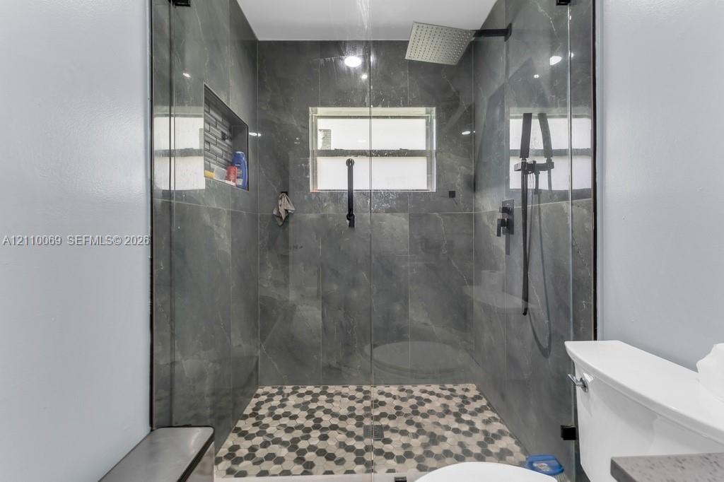 Walk-in shower featuring large-format dark stone-finish wall tile, a geometric hexagonal mosaic tile floor, an integrated wall niche, a frameless glass enclosure, and matte black plumbing fixtures