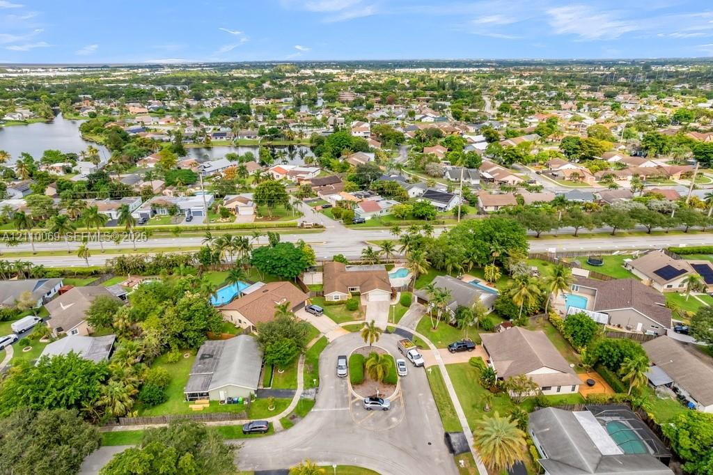 Aerial perspective of a residential community featuring a cul-de-sac, paved roadways, mature palm trees, and neighborhood lakes