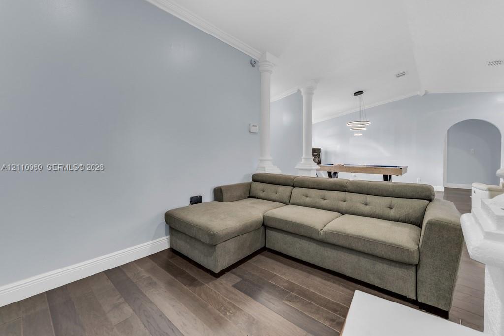 Interior space featuring wood-finish flooring, vaulted ceilings, decorative columns, arched doorways, and a modern tiered chandelier