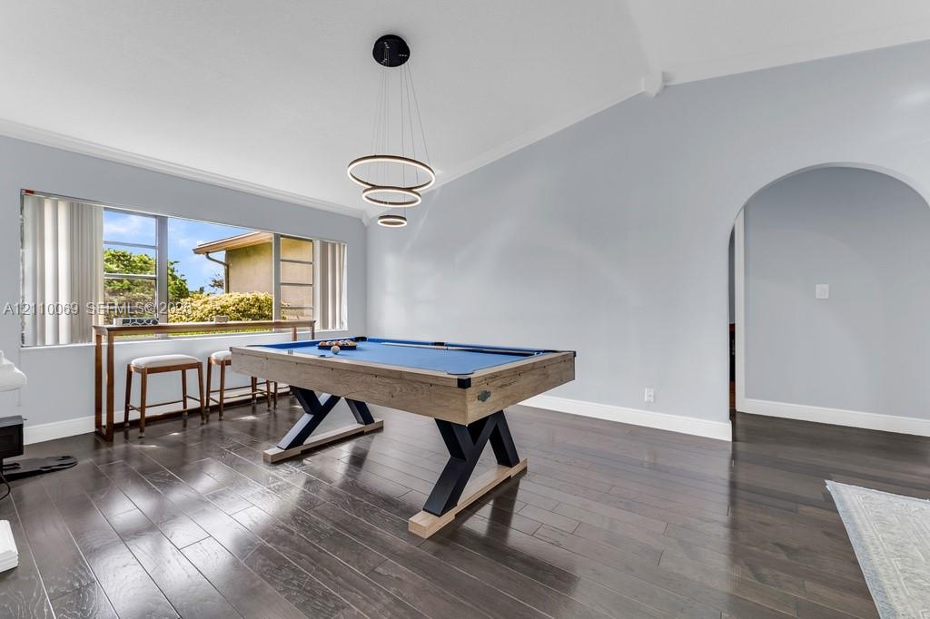 Vaulted ceilings, wood-finish flooring, architectural arched opening, triple-ring modern chandelier, and oversized window with natural light