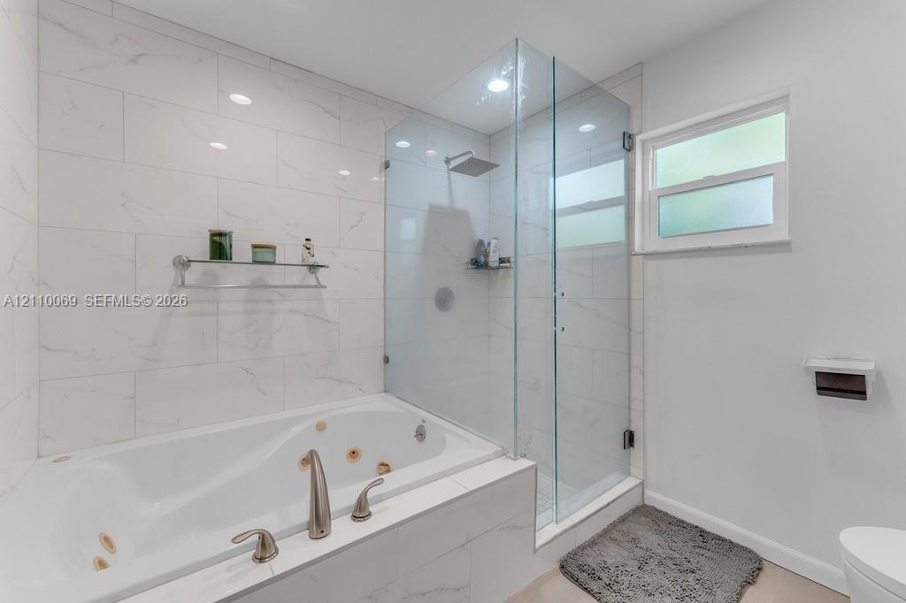 Jetted soaking tub, walk-in shower with a glass enclosure, oversized wall tiling, and a rainfall showerhead
