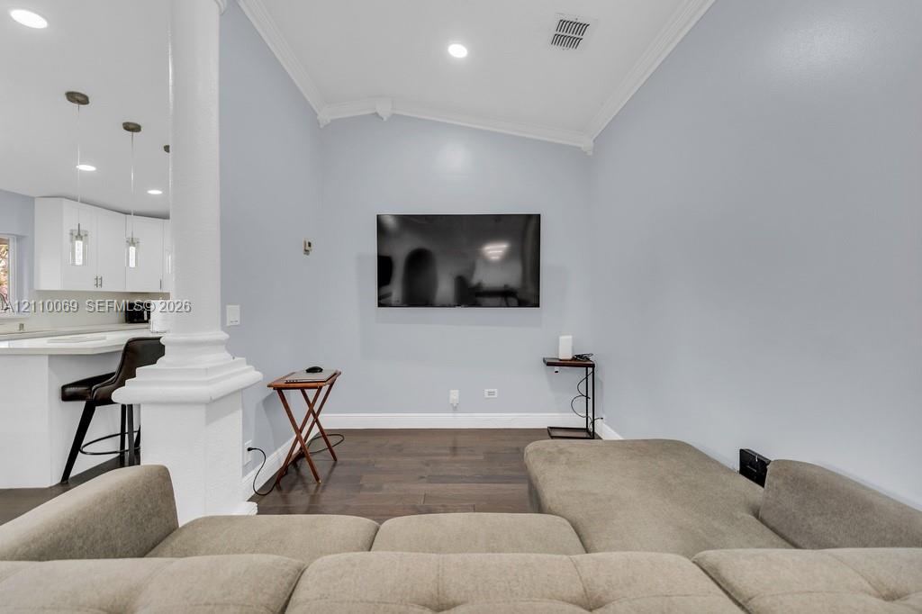Open concept area featuring dark wood-finish flooring, a classic column, recessed lighting, and crown molding