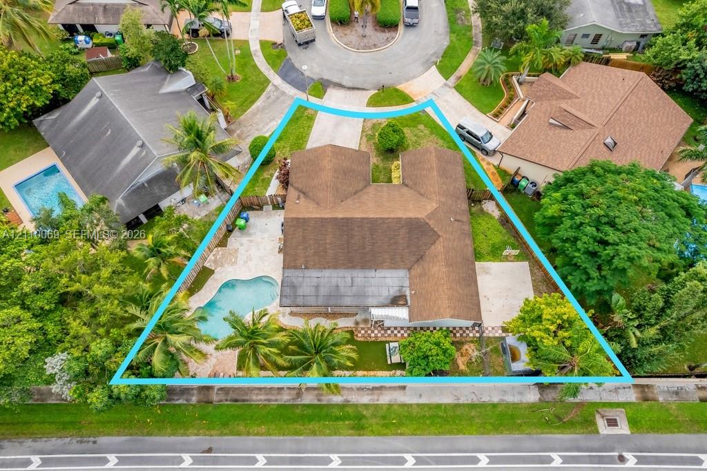Aerial view of a cul-de-sac lot featuring an in-ground swimming pool, concrete patio, mature landscaping, and a multi-gabled roofline