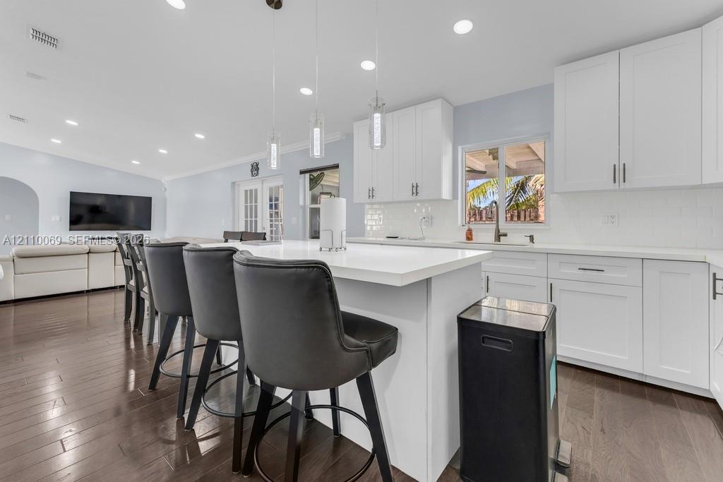 Kitchen featuring white shaker-style cabinetry, quartz countertops, a central island, recessed lighting, and wood-finish flooring