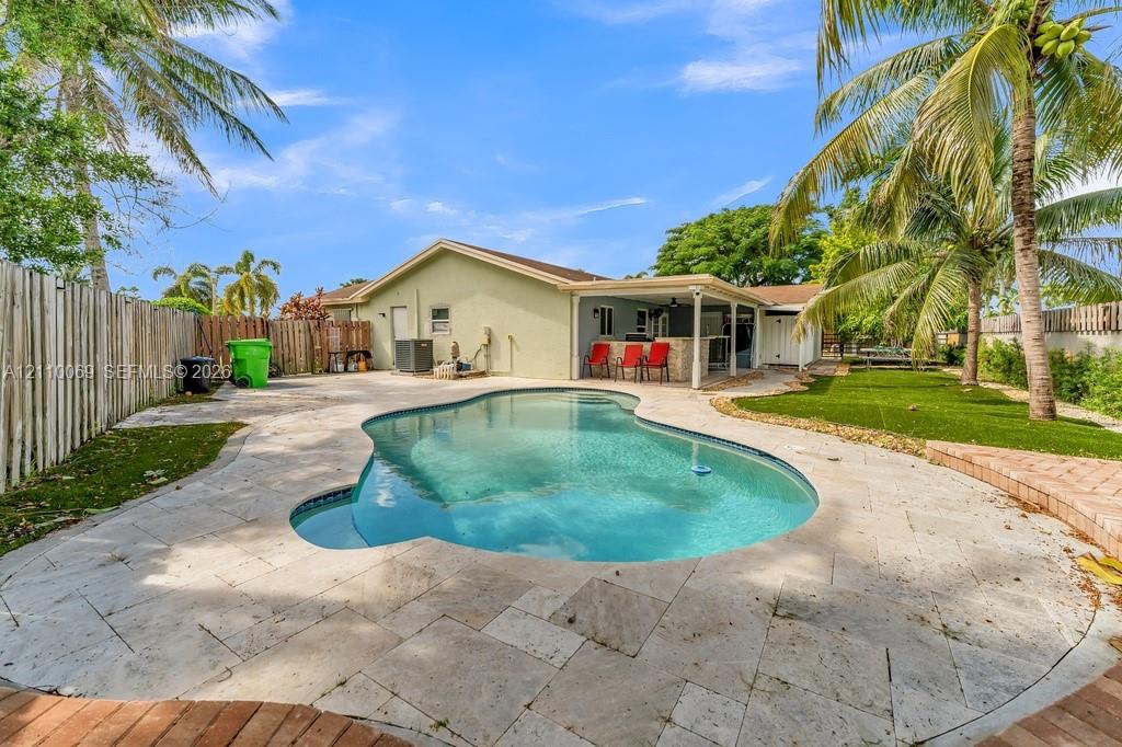 Backyard featuring a free-form pool, stone-paver decking, covered patio with a built-in outdoor bar, and a fenced perimeter