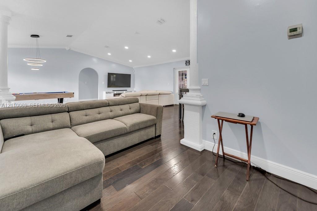 Open-concept room featuring wood-finish flooring, recessed lighting, architectural columns, and a rounded archway