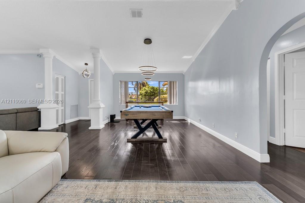 Open-concept interior featuring wood-finish flooring, architectural columns, a multi-tiered circular pendant light, and an arched doorway