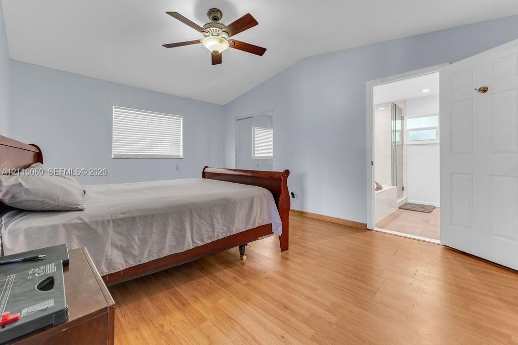 Bedroom featuring wood-finish flooring, vaulted ceilings, ceiling fan with integrated lighting, window blinds, and mirrored closet doors