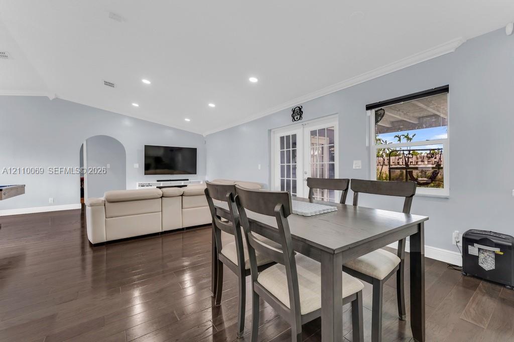 Open living space featuring dark wood-finish flooring, recessed lighting, crown molding, an arched entryway, and double French doors