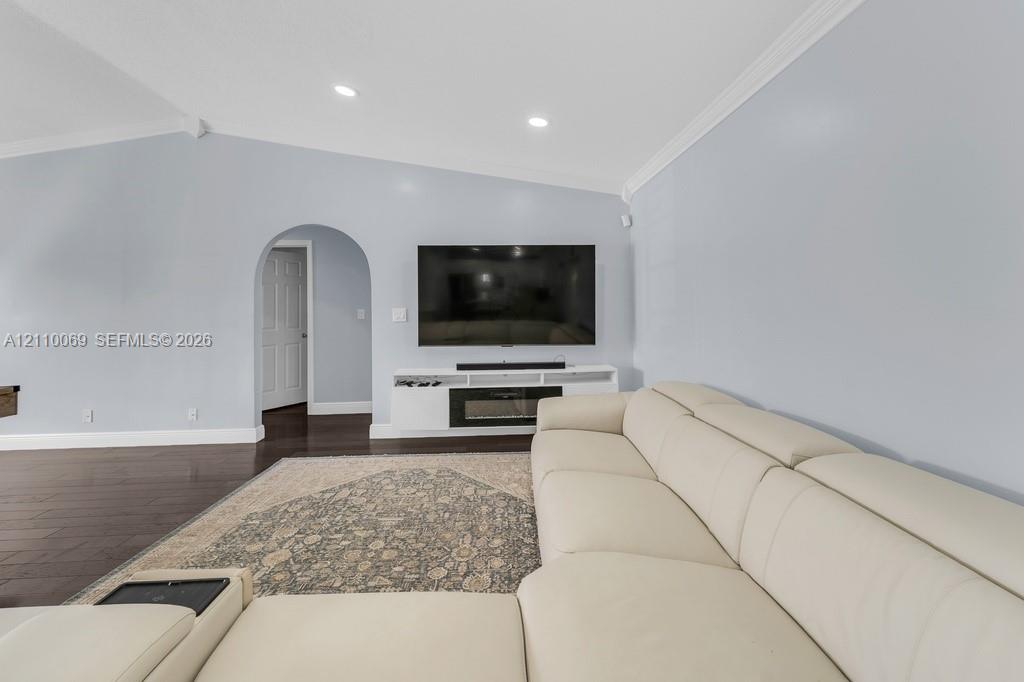 Vaulted ceilings featuring recessed lighting, dark wood-finish flooring, an arched doorway, and a built-in media console with an integrated fireplace