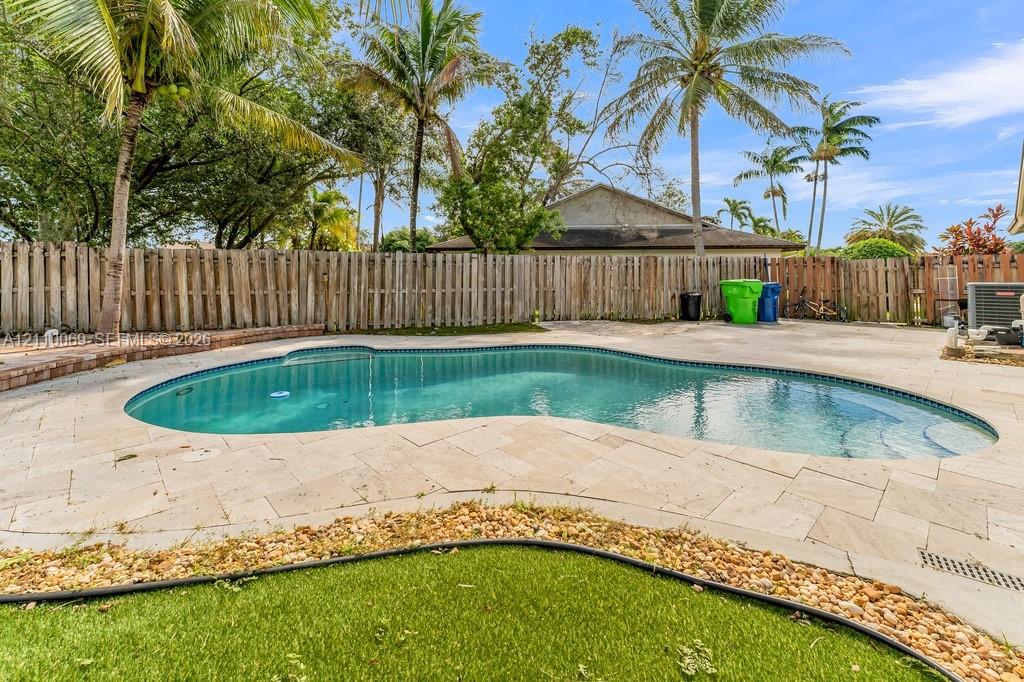 Freeform swimming pool with stone-tiled patio, stone curbing, wood-style privacy fencing, and established palm trees