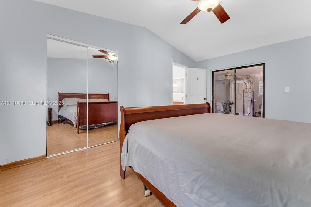 Vaulted ceiling featuring a ceiling fan with integrated lighting, wood-finish flooring, and floor-to-ceiling mirrored sliding closet doors