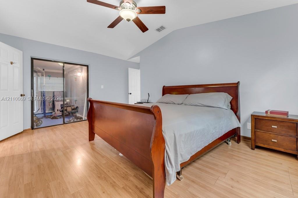 Vaulted ceiling with integrated wooden-finish ceiling fan, wood-finish flooring, and sliding glass mirror-panel closet doors
