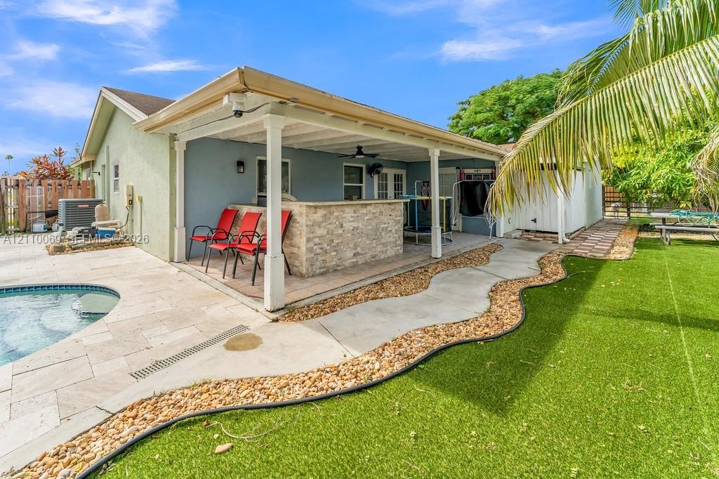 Covered outdoor patio featuring a stone-faced built-in bar, tile pool deck, swimming pool, and artificial turf lawn