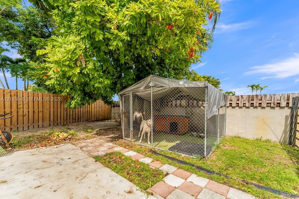 Private backyard featuring a fenced enclosure, concrete patio, decorative paver border, and mature perimeter trees