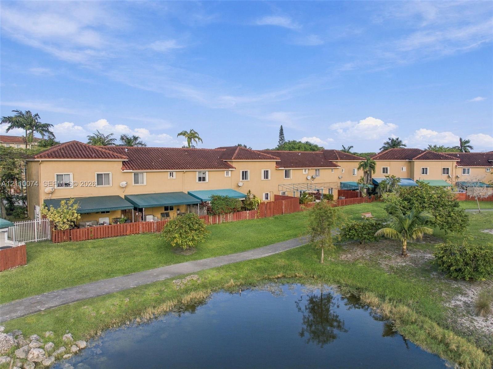 Multi-story stucco exterior featuring a tile roof, dedicated green space, paved pathways, and a water feature