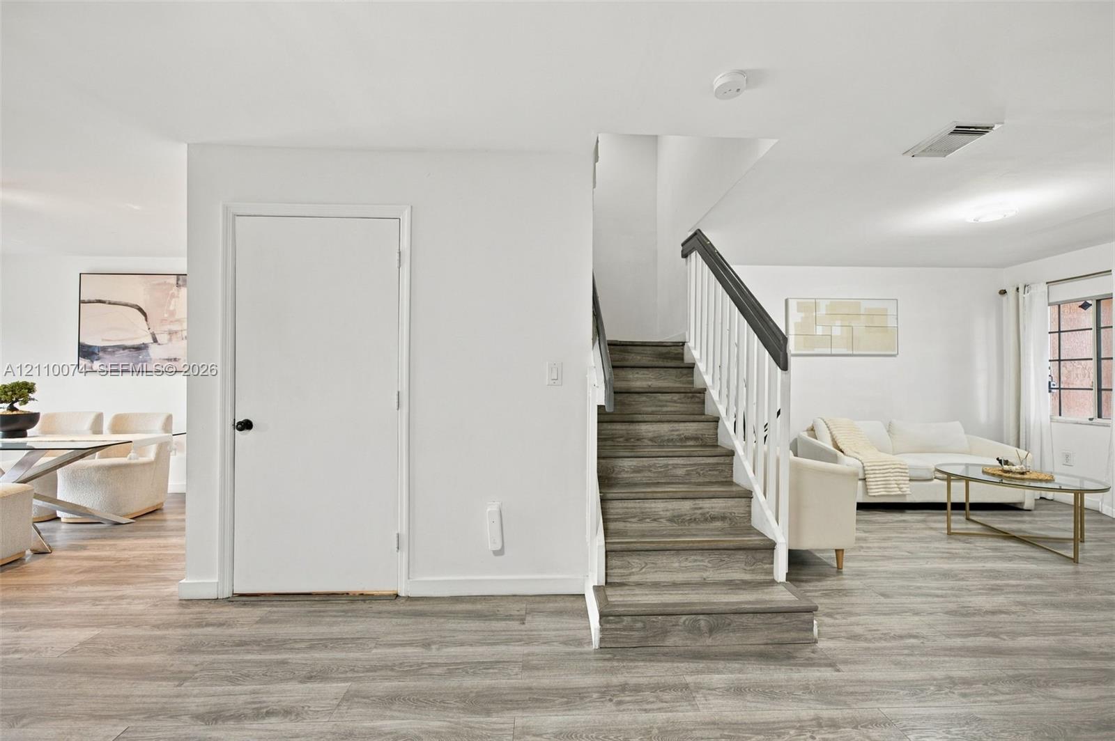 Staircase featuring white balusters and a dark-toned handrail, wood-finish flooring, and a multi-pane window