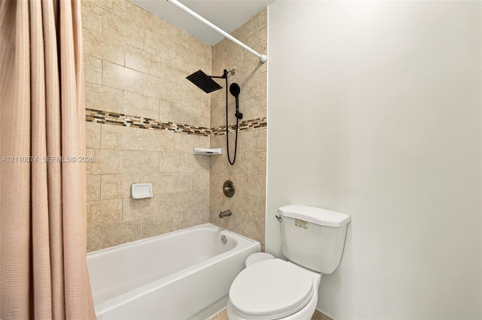 Full bathroom featuring a shower-tub combination with large-format wall tile, decorative tile inlay, a matte black rainfall showerhead, and a matching handheld sprayer