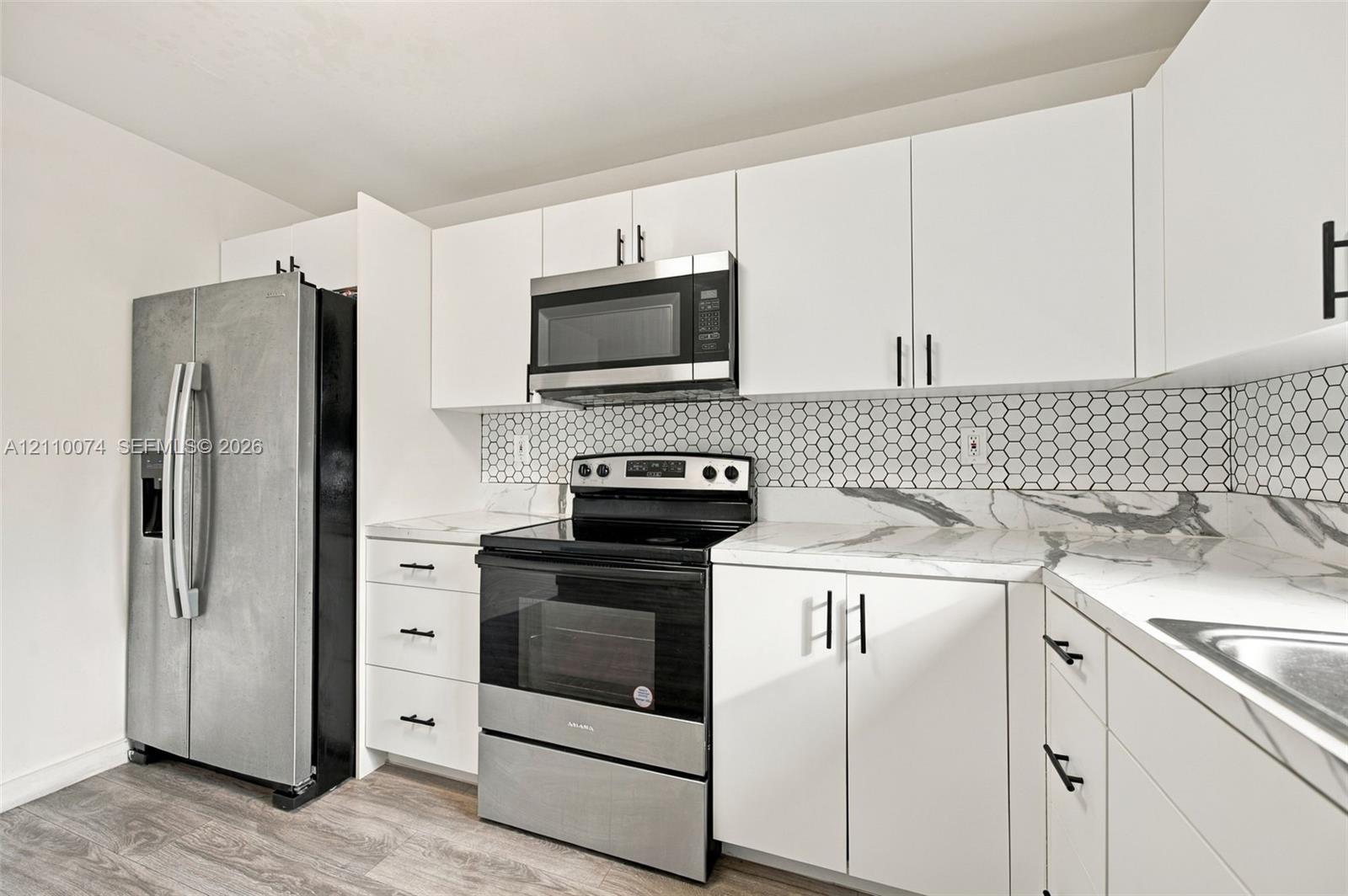 Kitchen featuring white cabinetry, stone-look countertops, hexagonal tile backsplash, stainless steel appliances, and wood-finish flooring