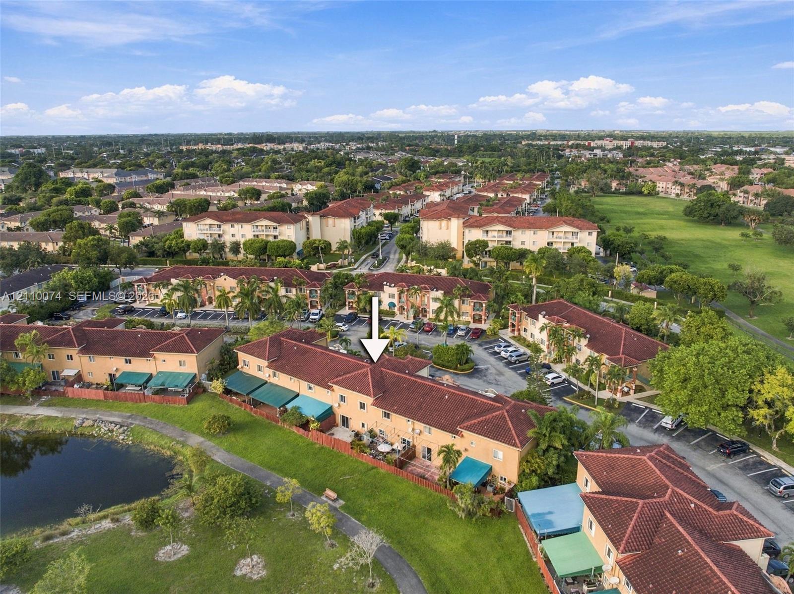 Aerial perspective of a multi-unit residential complex featuring terracotta-style roofing, stucco exterior finish, paved surface parking, and a waterfront location with mature landscaping