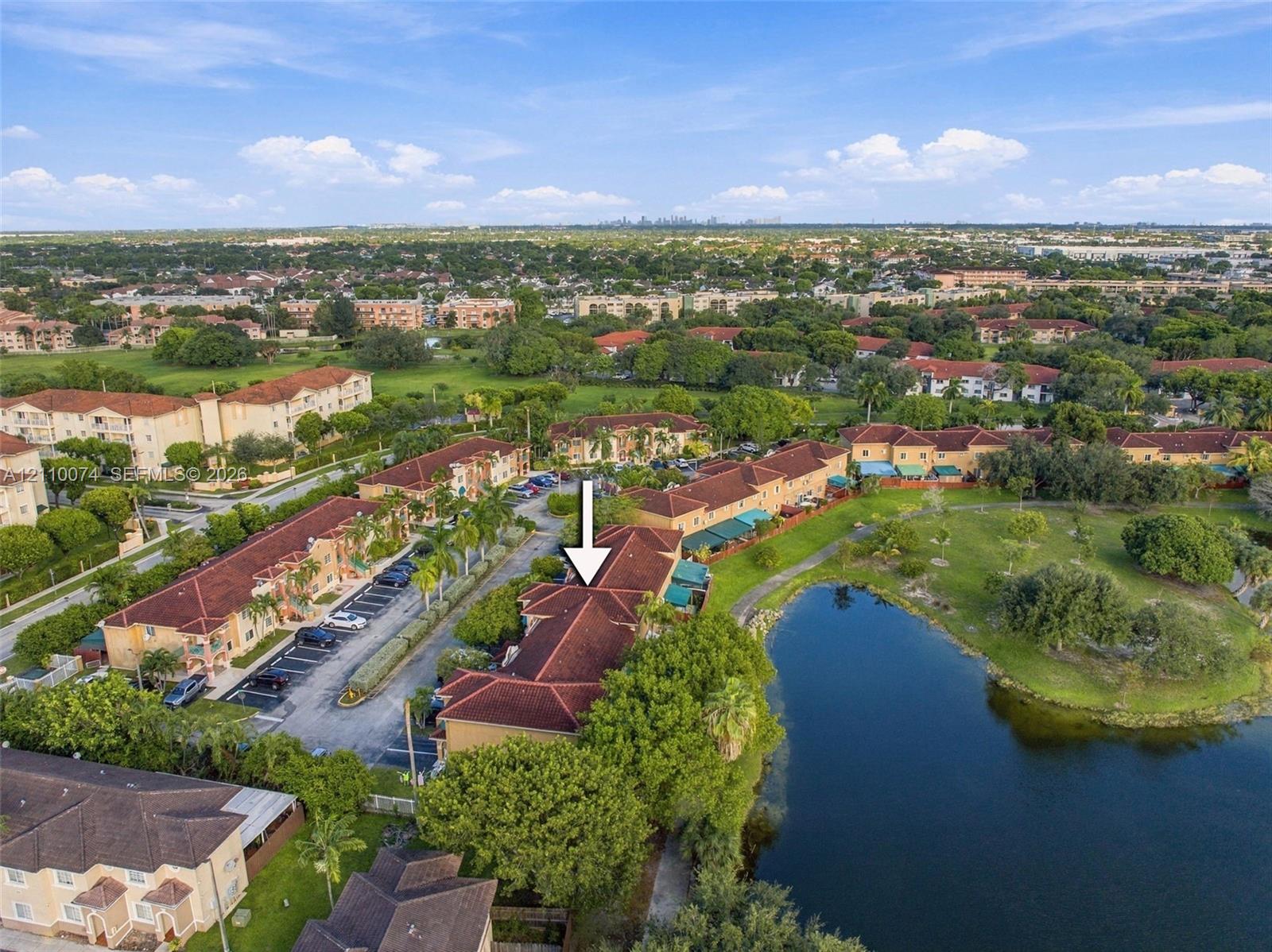 Aerial perspective of a multi-unit residential structure featuring a terracotta-style tiled roof, expansive water frontage, mature perimeter landscaping, and dedicated asphalt parking