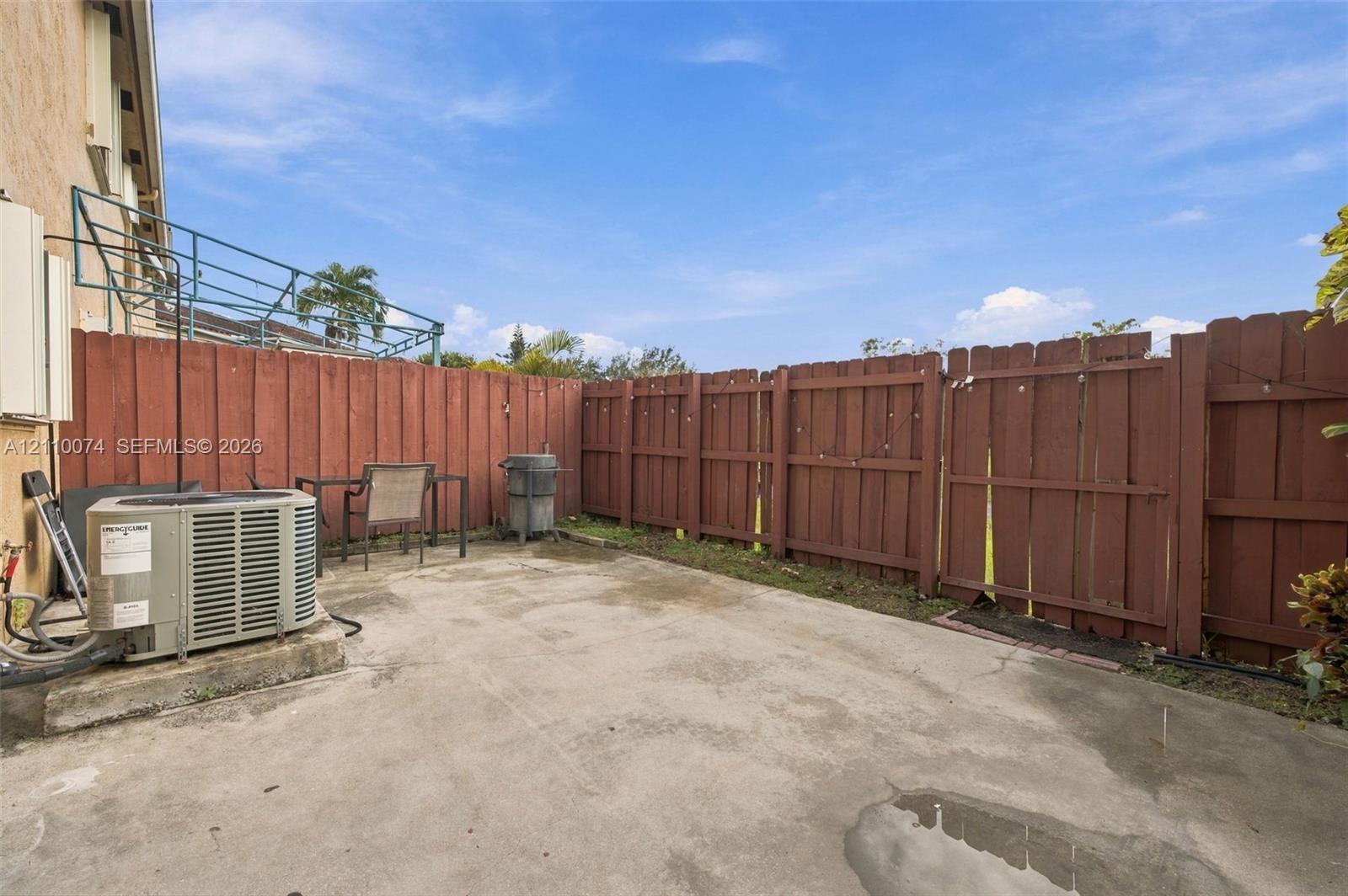 Rear concrete patio enclosed by a perimeter wood-slat fence