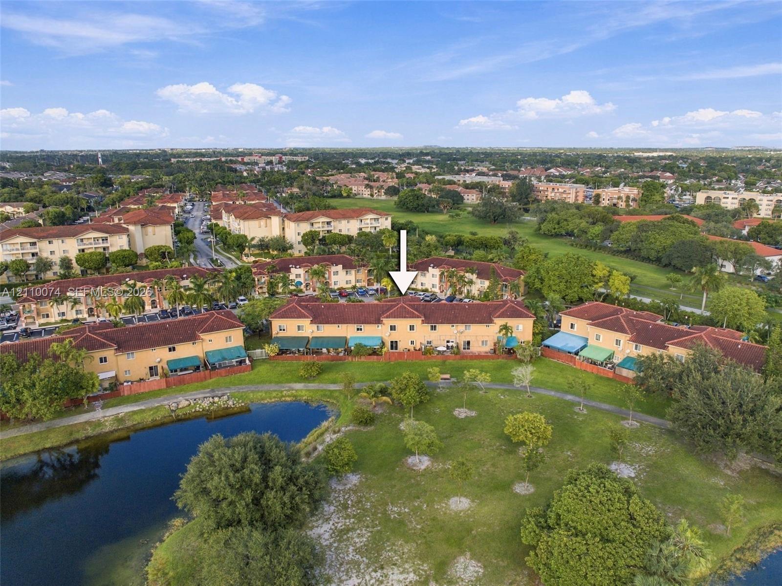 Aerial perspective of a multi-unit complex featuring terra cotta-style shingle roofing, stucco exterior, and waterfront grounds with a paved walking path