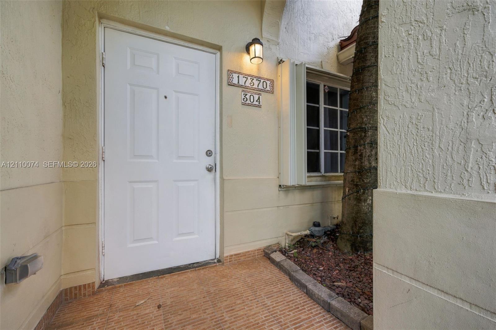 Stucco exterior entryway featuring a six-panel door, masonry tile flooring, recessed wall-mounted lighting, and a multi-pane window