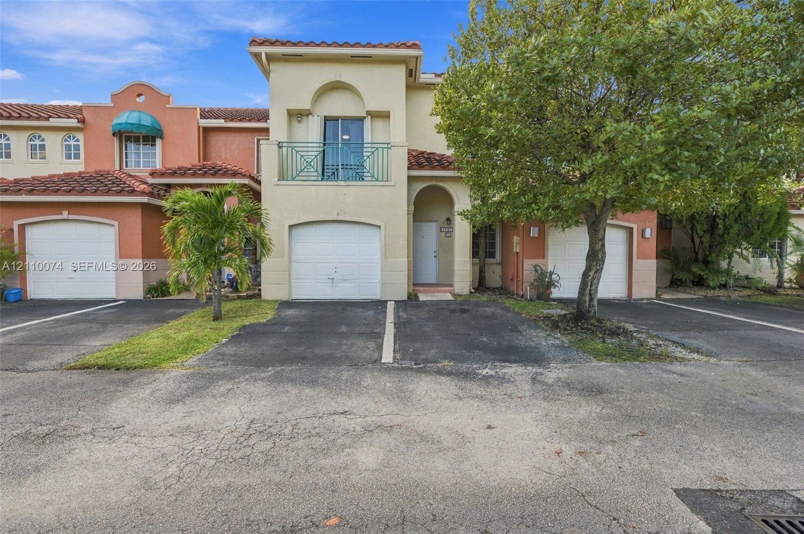 Mediterranean-inspired townhome featuring a stucco exterior, clay tile roofing, private upper-level balcony with metal railing, and attached garage Mediterranean-inspired townhome featuring a stucco exterior, clay tile roofing, private upper-level balcony with metal railing, and attached garage