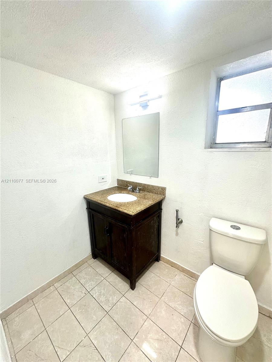 Dark wood-finish vanity with a stone-surface countertop, integrated white sink, rectangular mirror, and ceramic tile flooring