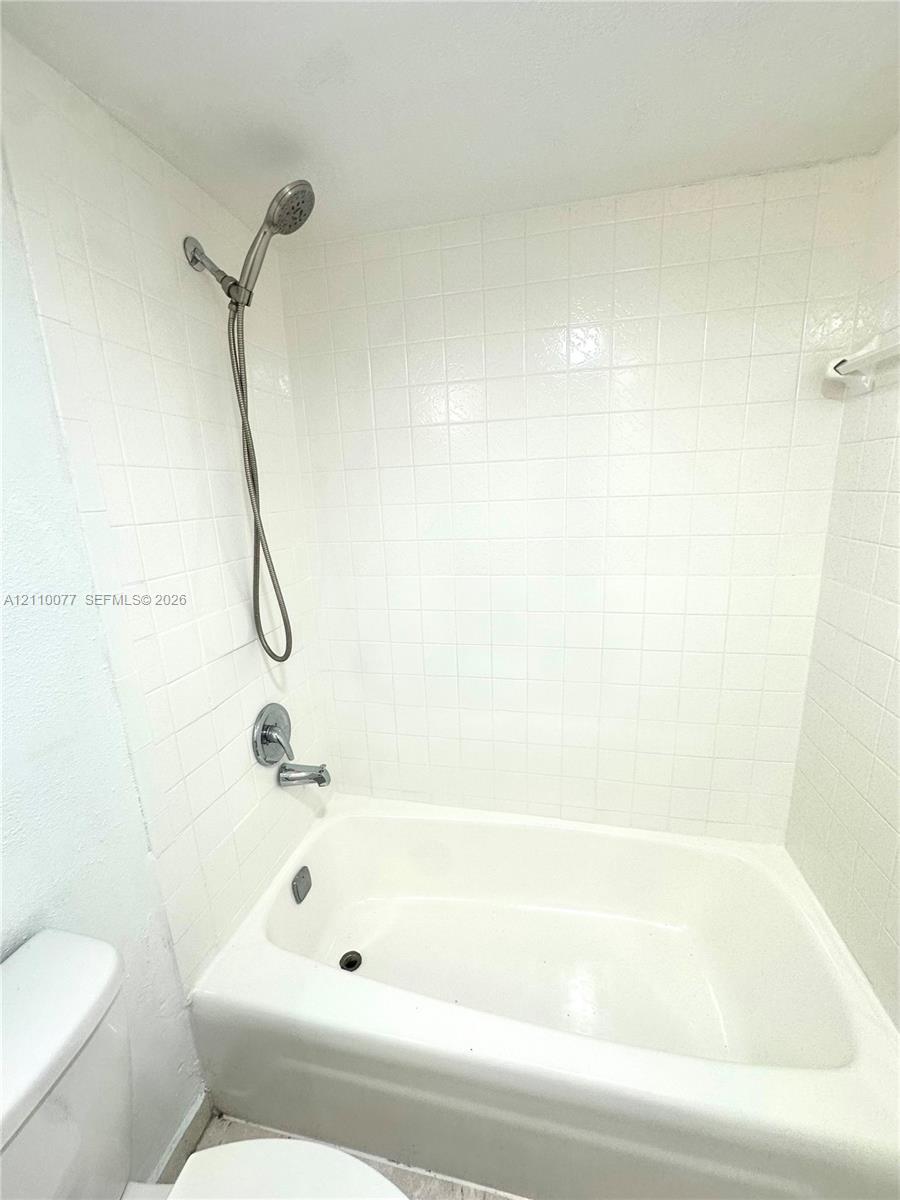 Full-height white square tile surround, tub-shower combination with a handheld shower fixture, and polished metal plumbing hardware