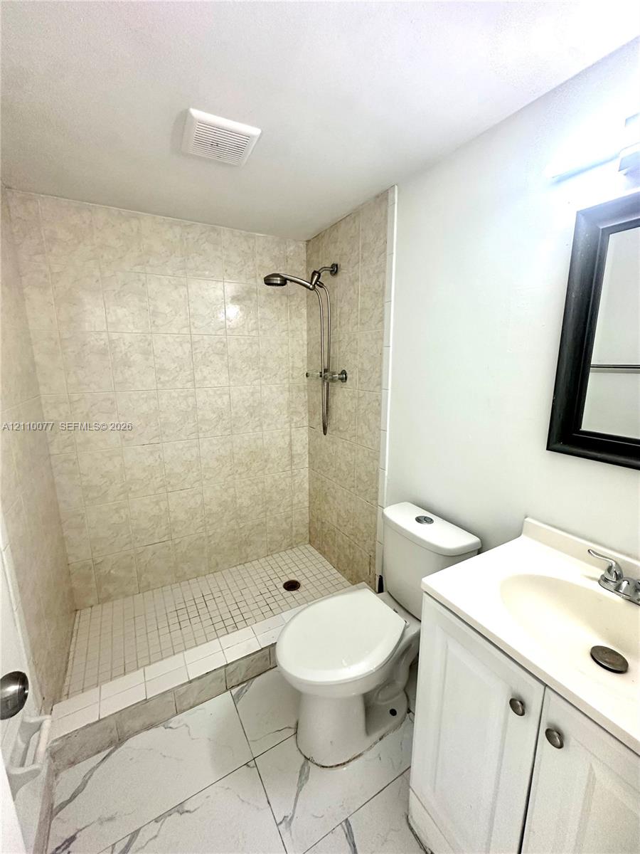 Walk-in shower with stone-patterned wall tile, white vanity featuring a molded sink, and large-format tile flooring with marble-style veining