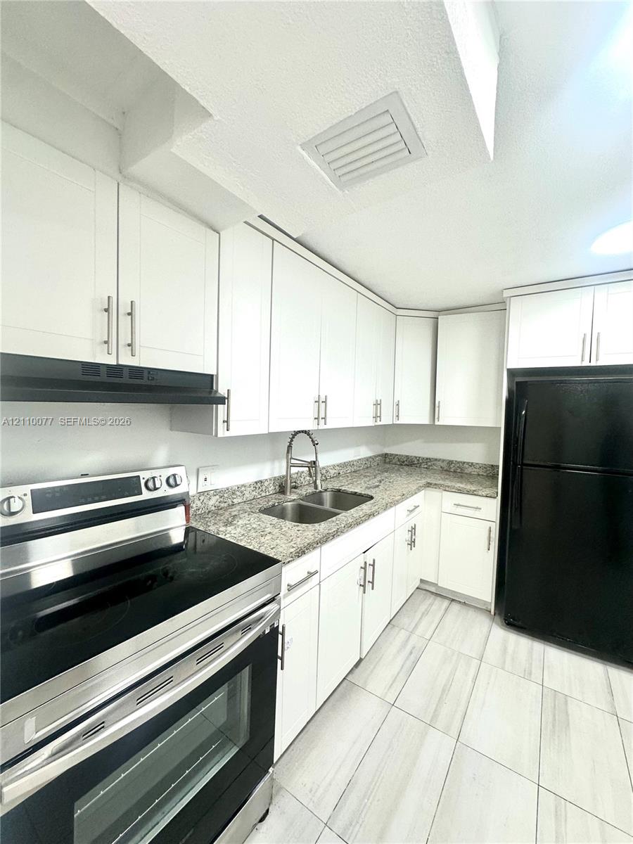Kitchen featuring white shaker-style cabinetry, stone-finish countertops, dual-basin stainless steel sink with high-arch faucet, and large-format tile flooring